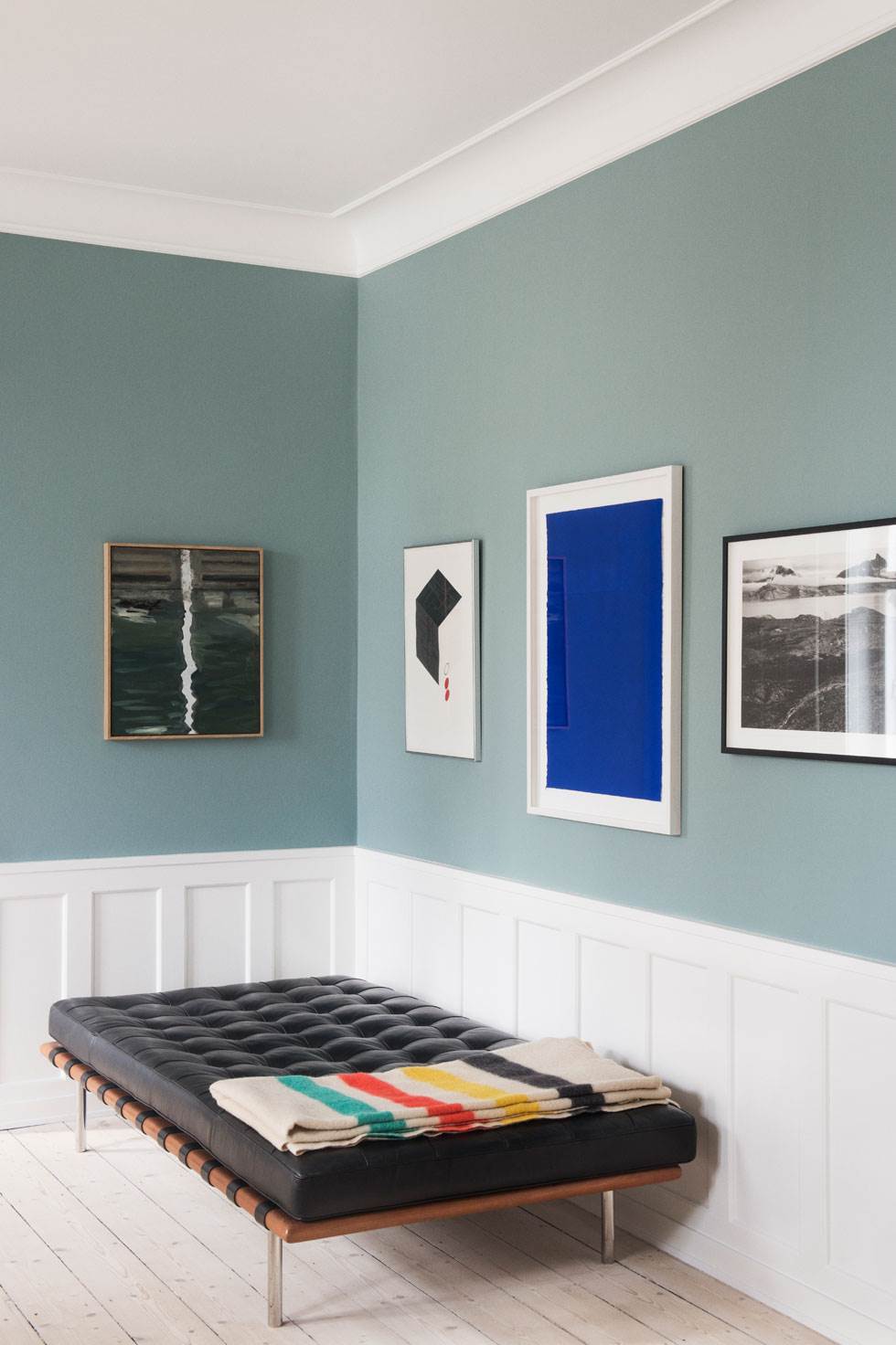 Væggen er malet med Oval room blue fra Farrow and Ball. Det grønne maleri er af Anne Berger, litografi af Schwalbe, det blå værk af Anders Bülow, og fotoet af Per Bak Jensen fik Trine i 30 års fødselsdagsgave af sine forældre. Daybed Barcelona er hjembragt fra New York, og plaiden er et loppefund. Foto: Gyrithe Lemche